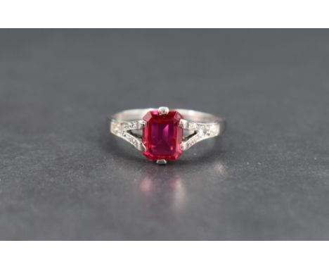 A synthetic ruby and diamond ring, the emerald cut ruby measuring approximately 1ct in a claw set mount to diamond set split 