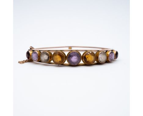 A 9ct yellow gold victorian bangle,
set with semi-precious stones,
quartz citrine amethyst and garnet,
13.6 grams in weight a