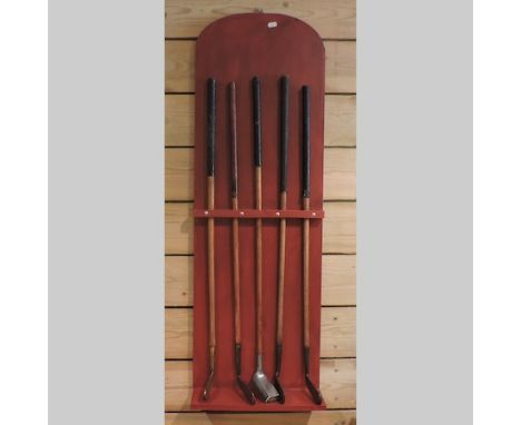 A collection of five early 20th century hickory shafted golf putters, to include James Braid, R. Simpson, on a painted stand
