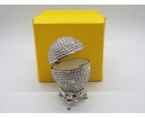 A crystal encrusted egg form trinket box with white enamel interior, with display stand and contained in original box, approx