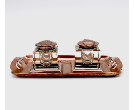 An Aesthetic Movement copper inkstand, circa 1900, with pierced grips and fitted two copper topped glass inkwells, width 17.5