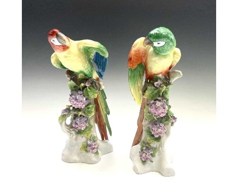 A pair of Continental porcelain figures of parrots, circa 1900, with brightly coloured plumage on flower encrusted tree trunk