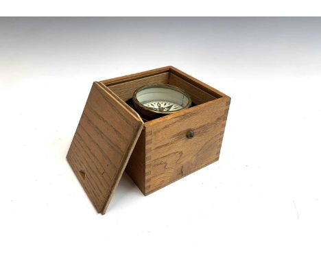 An unmarked brass compass in a cast metal gimbal within an oak case, 7.8cm diameter.