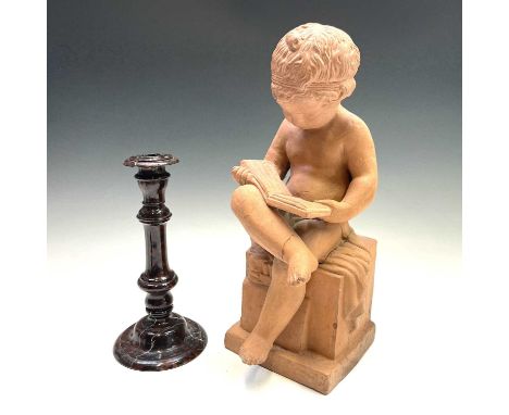 A Cornish serpentine candlestick, height 27cm, together with a terracotta figure of a boy, seated reading a book, height 43cm