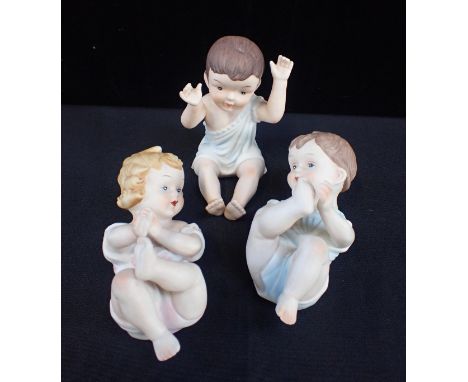 THREE BISQUE PIANO BABIESthe pair 14cm long, and the single seated 12cm high