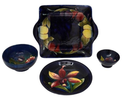Four pieces of Moorcroft pottery comprising a 'Wisteria Plum' square twin handled serving plate, c1918-1929, blue ground, imp