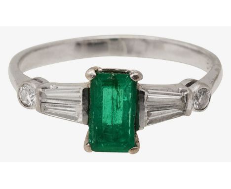 An emerald and diamond ring rectangular step-cut emerald, between tapered-baguette cut diamond set shoulders, terminating in 