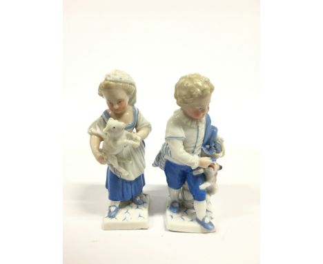 A pair of Dresden figures modelled as a young girl and boy tending a puppy and a lamb in tones of blue and white with painted