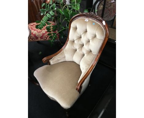 A Victorian style spoon back nursing chair resting on cabriole legs to castors to front with a button back fabric upholstered