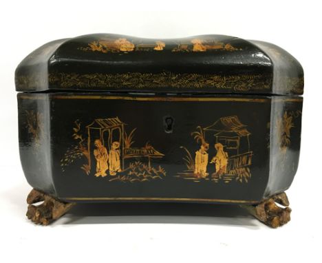 A Chinese lacquer style tea caddy decorated with figures and flowers in gilt resting on gilt wood carved lions paw feet.