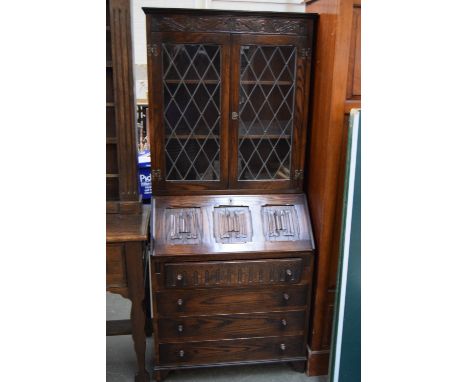 A Jacobean style bureau with carved cornice over cupboard with glazed leaded glass double doors, drop down carved flap, inter