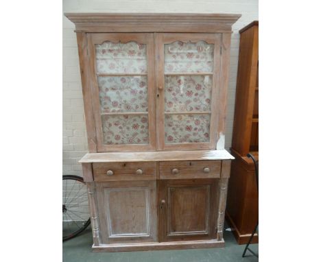 A large pine dresser with stepped cornice over a cupboard with a pair of glazed doors hung with internal floral curtains and 