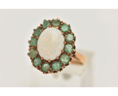 A 9CT GOLD OPAL AND EMERALD RING, a cabochon oval opal, prong set with a surround of circular cut emeralds, approximate lengt