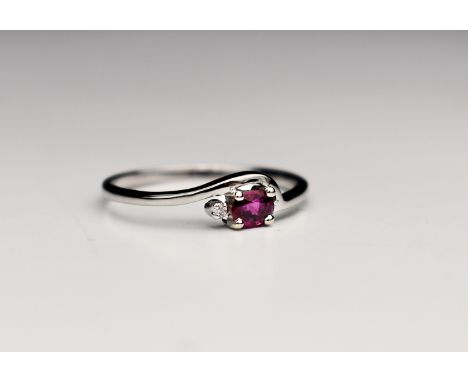 An 18ct white gold, ruby and diamond ring, the oval cut ruby beside a single brilliant cut diamond in a dainty cross over set