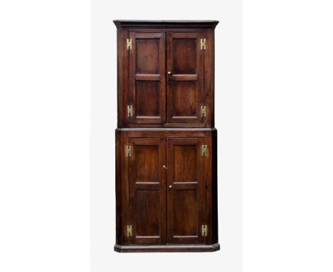 A George III joined oak two-part floor standing corner cupboard, the stepped pediment over a pair of two panel doors on brass