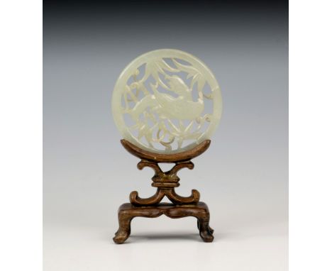 A Chinese carved and pierced celadon jade disc on stand, depicting a bird in foliage, 2¼in. (5.5cm.) diameter.
