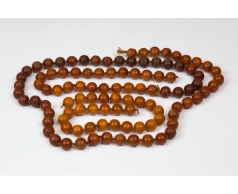 Two amber bead necklaces, early 20th century, both with circular, 13mm. evenly sized beads, the shorter necklace with lighter