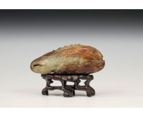 A Chinese jade carving of a carp and lotus leaf, the pale celadon and red brown mottled jade depicting a carp half-hidden wit