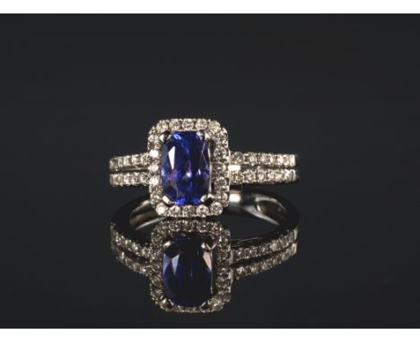 An 18ct white gold, Tanzanite and diamond cluster ring, the 7.5 x 5mm. cushion cut Tanzaite within a halo border of brilliant