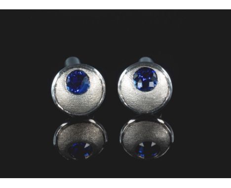 A pair of 18ct white gold and sapphire cufflinks, the matted gold discs set off-centre with a single round cut sapphire of go