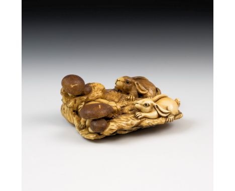 A Japanese carved ivory netsuke, Meiji period (1868-1912), with three leverets playing amongst toadstools, on naturalisticall