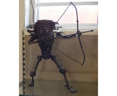 A figure of an alien firing a bow and arrow made from car parts, 45 cm tall