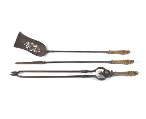 A set of three 'Egyptomania' steel and brass mounted fire tools, 19th century, comprising shovel, poker and tongs, the grips 