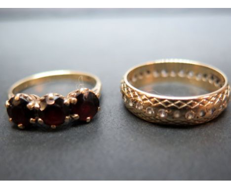 Two 9ct gold rings - To include a garnet three-stone, size O - Together with a white-gem full-circle ring, size R - Both with