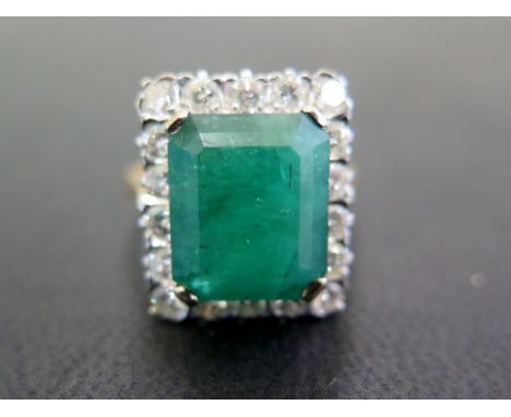 An emerald and diamond cluster ring - The octagonal emerald within a brilliant-cut diamond surround, to the plain band - Esti