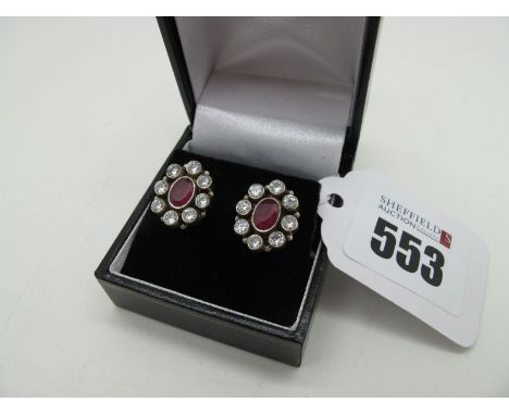A Pair of Modern Ruby Set Earrings, oval collet rubover set to the centre, within border of circular collet set highlights, o