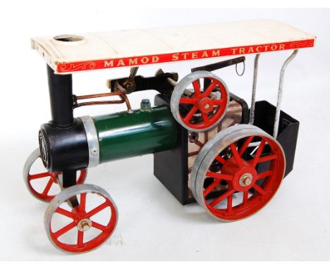 A Mamod live steam traction engine comprising green body with red spoked wheels and a cream canopy with steering rod, scuttle