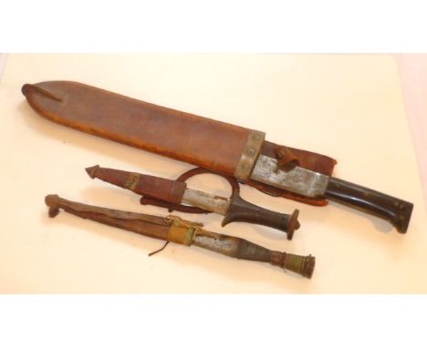 Two tribal daggers in leather sheaths together with a larger machete blade in leather sheath