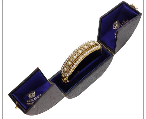 A late Victorian gold, diamond and half pearl hinged bangle, the upper section centred with half pearls spaced by pairs of ro