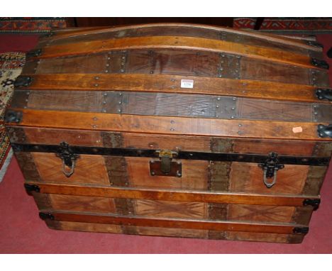 An early 20th century wooden leather and metal bound domed hinge-top travelling trunk, having fitted interior and leather end
