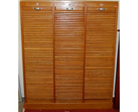 A 1930s light oak triple division tambour fronted office filing cabinet, enclosing a lined and shelved interior with two keys