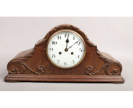 An 8 day oak cased dome top mantle clock decorated with scrolls.