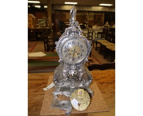 A late 19th Century mantel clock in ornate cast white metal case, surmounted by a putti holding bunches of flowers, fitted a 