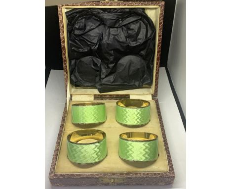 A BOXED SET OF FOUR HALLMARKED BIRMINGHAM NAPKIN RINGS WITH GREEN ENAMEL DECORATION 