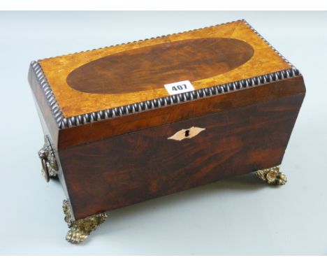 A Regency mahogany tea caddy with gilt metal ring carrying handles and hairy paw corner feet, the burr walnut top with oval c
