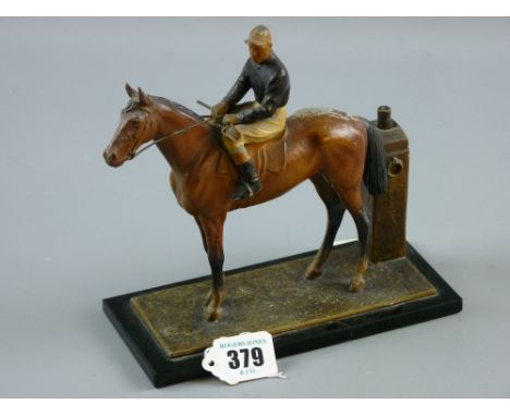 A spelter cold painted figure table lighter of a racehorse with a jockey up on a black glass base (fractured), the tethering 