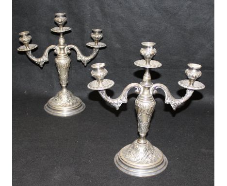 A pair of late 19th Century / early 20th Century white metal three light two branch candelabra with all-over embossed floral 