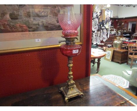 A Victorian brass oil lamp with cranberry shade and sump, 61cm high 
