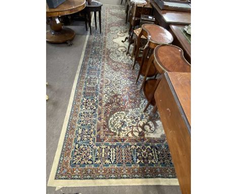 A large mid 20th Century machine made floor rug decorated with a large central floral panel on a principally pale background 