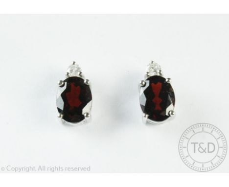 A pair of garnet and diamond set earrings in 14ct white gold, designed as an oval garnet below a diamond drop, post and butte