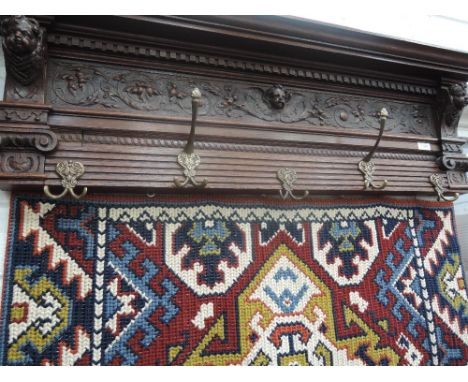 A late Victorian oak hall coat rack having carved foliate and mask decoration with later woodwork tapestry hanging