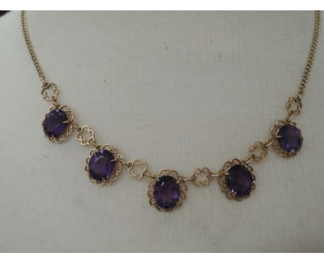 A yellow metal necklace stamped 375 having 5 amethyst style oval stones in decorative scroll mounts,  approx 12.5g