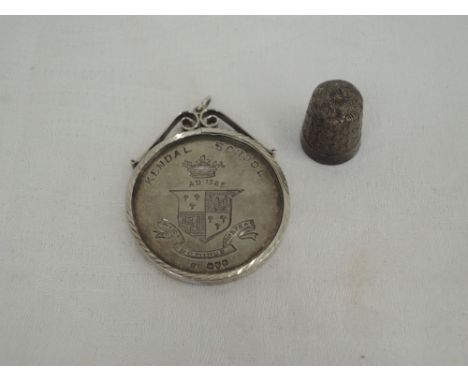 An HM silver commemorative coin regarding Kendal School awarded to F K Ion in a white metal surround stamped silver, and an H