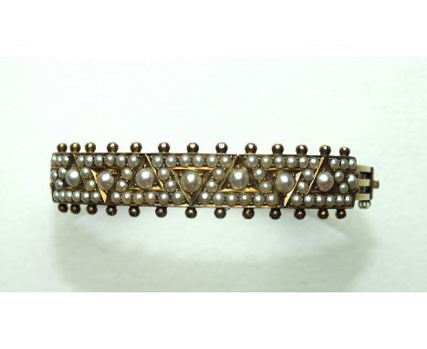 A late-19th century hinged bangle, the front set seed pearls within a geometric pattern, the back three parallel carved bars,