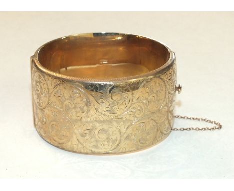 A 1960's 9ct gold hinged bangle with engraved scroll decoration, 3.7cm wide, 70g.