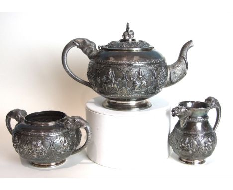 An Indian silver three-piece tea service of circular compressed form, heavily-embossed with panels of deities and having elep